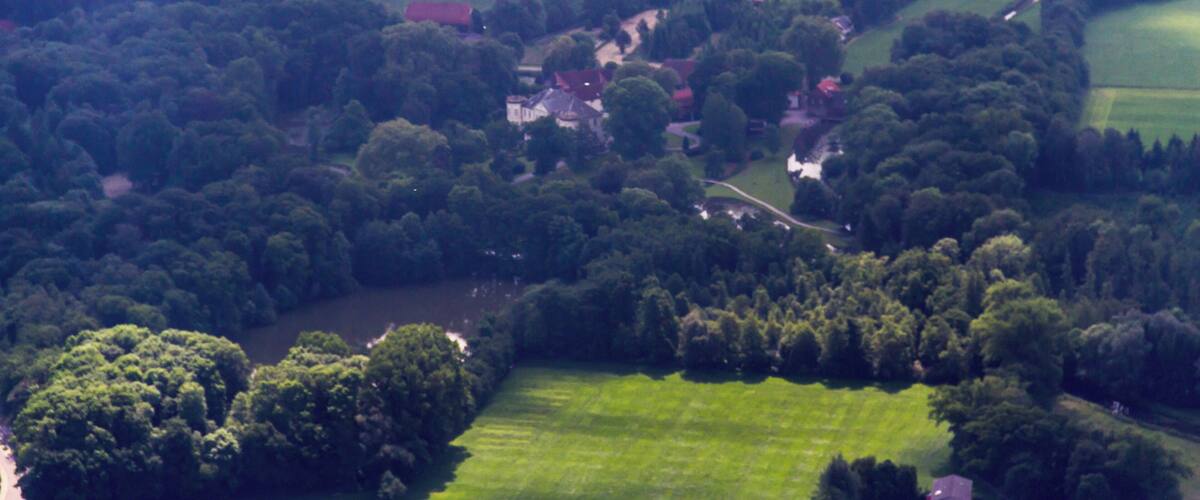 A lush green landscape with rolling hills, dense forests, and scattered houses.