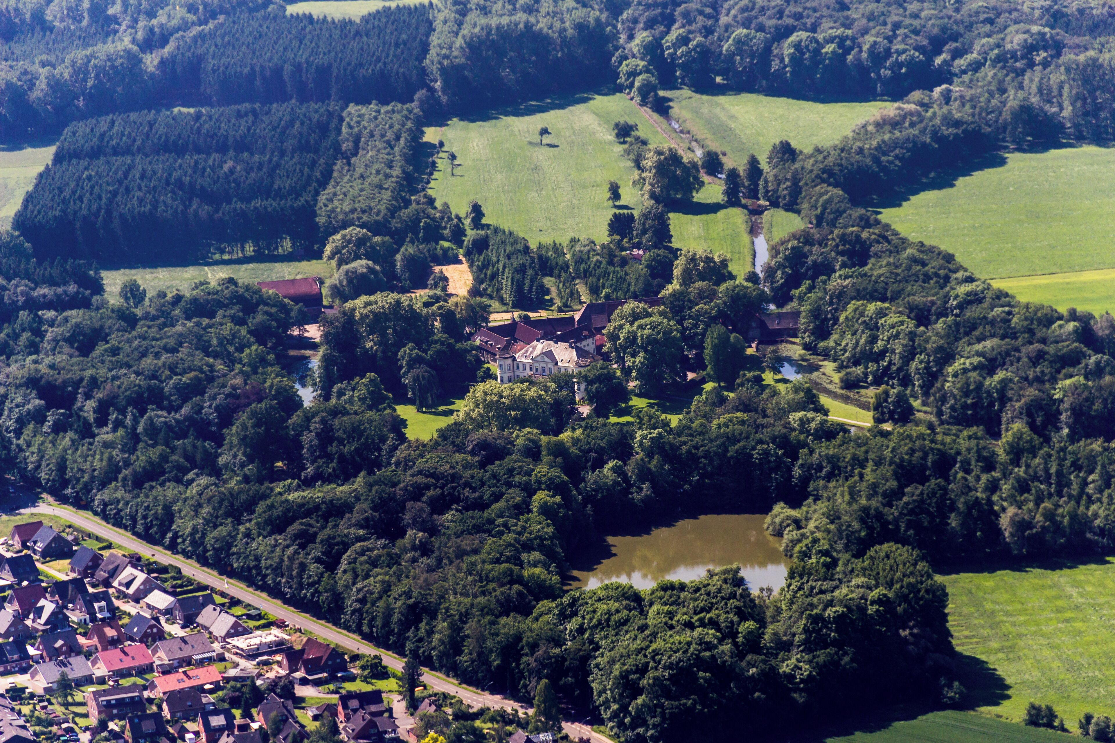 An aerial view of a village with houses, a pond, and surrounding greenery.