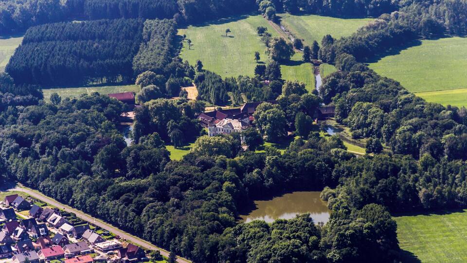 An aerial view of a village with houses, a pond, and surrounding greenery.