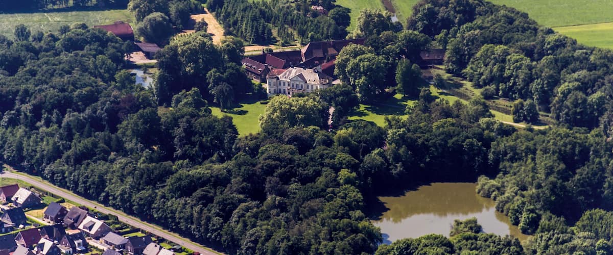 Une vue aérienne d’une zone rurale avec un vaste domaine entouré de forêts denses, un petit lac et des maisons dispersées.