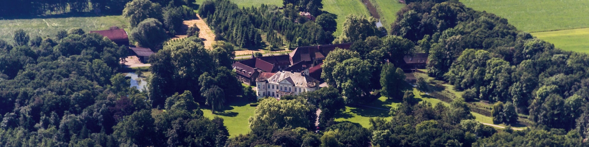 An aerial view of a rural area with a large estate surrounded by dense forests, a small lake, and scattered houses.