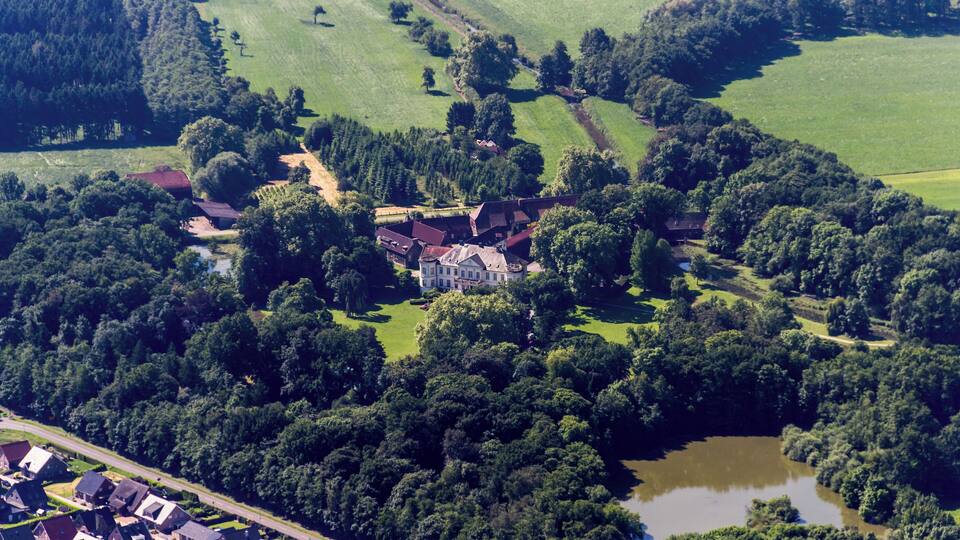 An aerial view of a rural landscape with a large estate surrounded by dense forests and a small lake.
