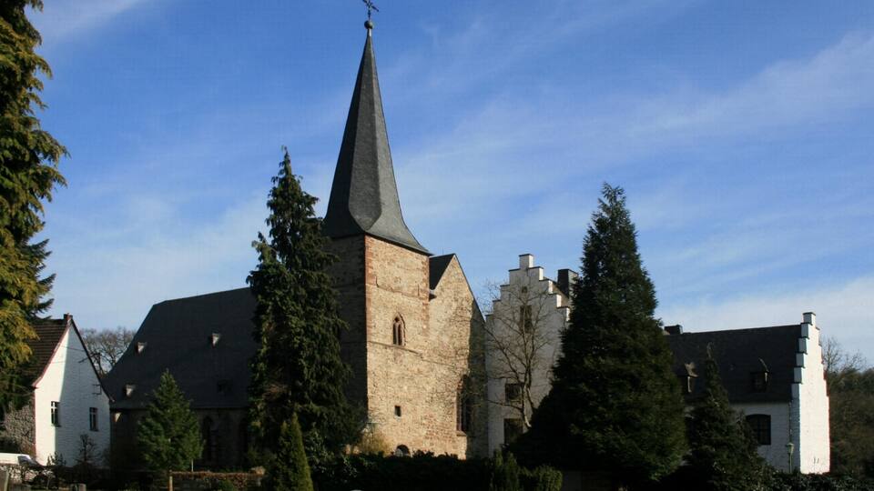 A church with a tall steeple, surrounded by trees and a well-maintained garden.