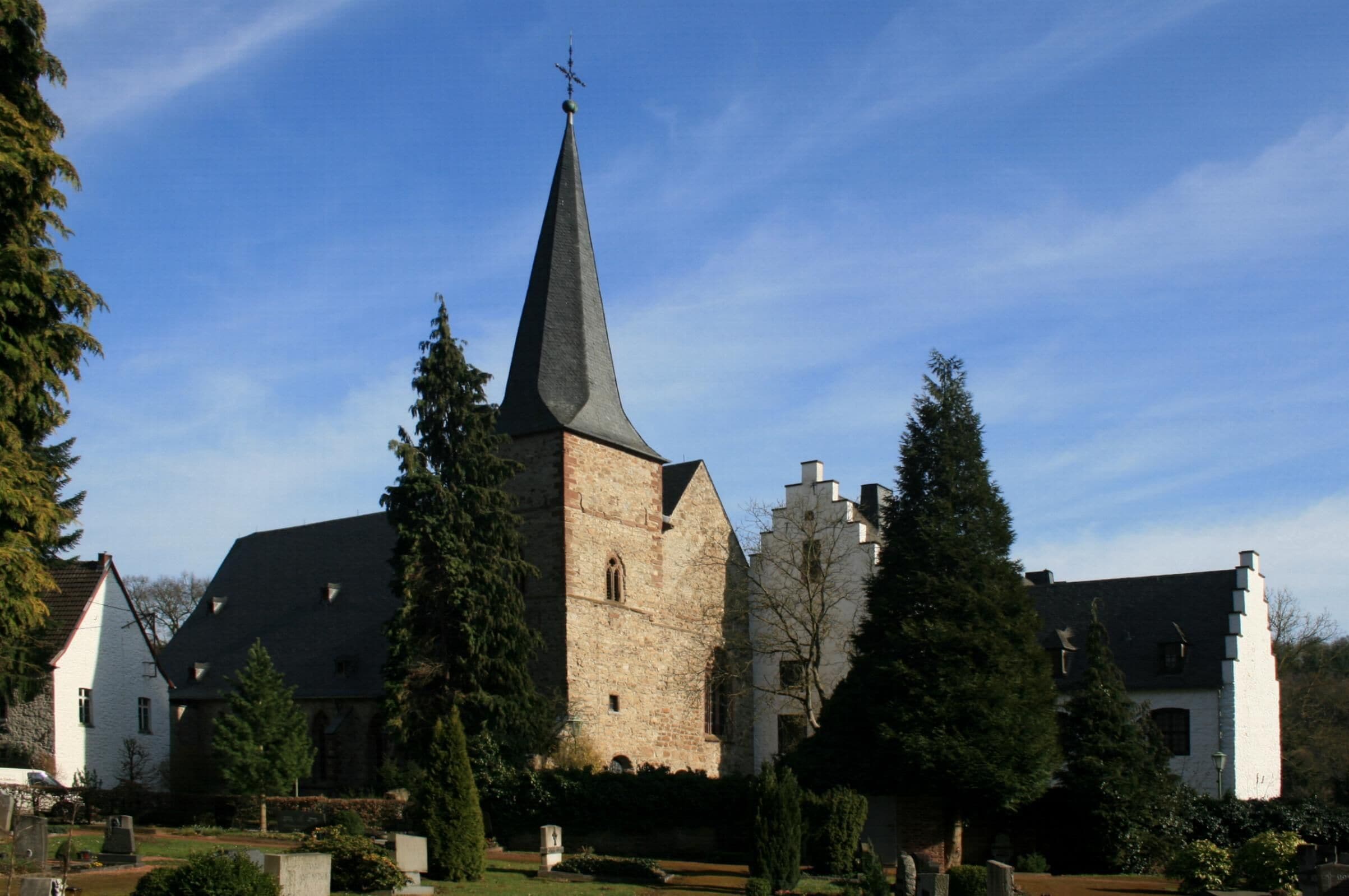 A church with a tall steeple, surrounded by trees and a well-maintained garden.