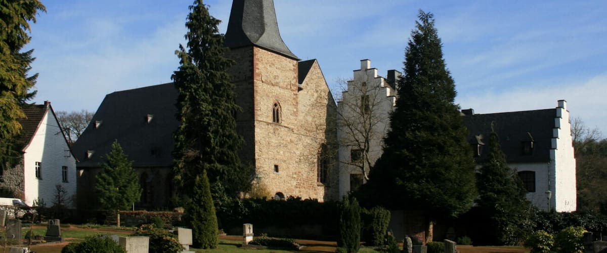 A church with a tall steeple, surrounded by trees and a well-maintained garden.