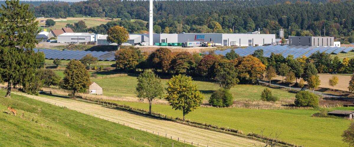 A wind turbine, solar panels, and industrial buildings in a rural landscape.
