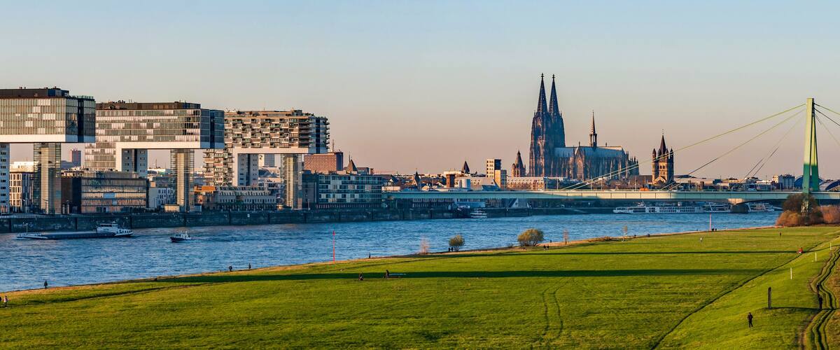 Ein Fluss mit Booten, ein grüner Park und eine Stadtansicht mit modernen Gebäuden und einem historischen Dom.
