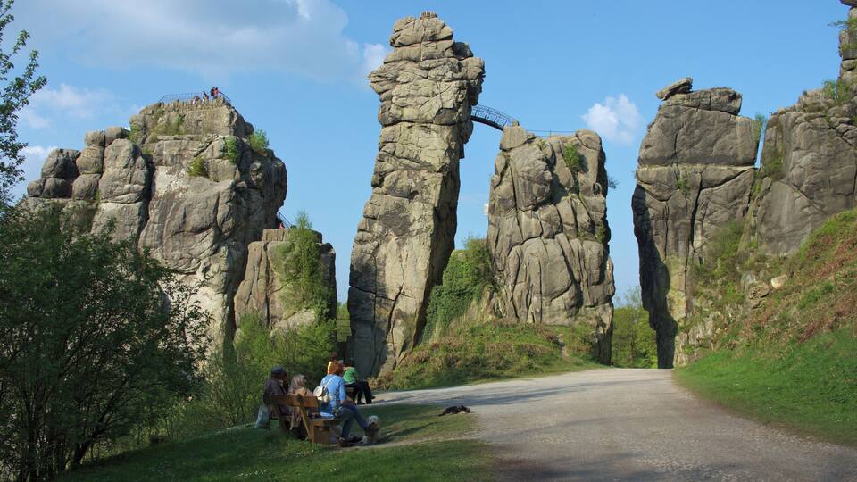 A road leading through a rocky landscape with large rock formations and a few people sitting on benches.