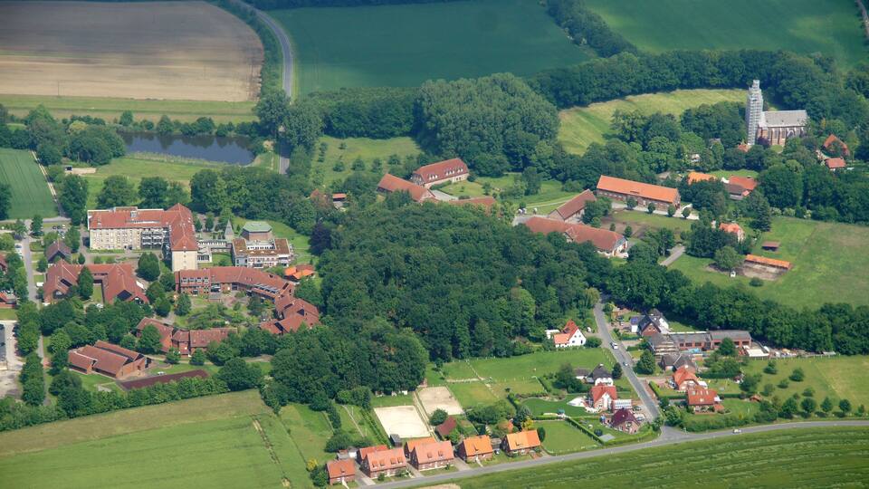 An aerial view of a rural village with houses, a church, and surrounding fields.