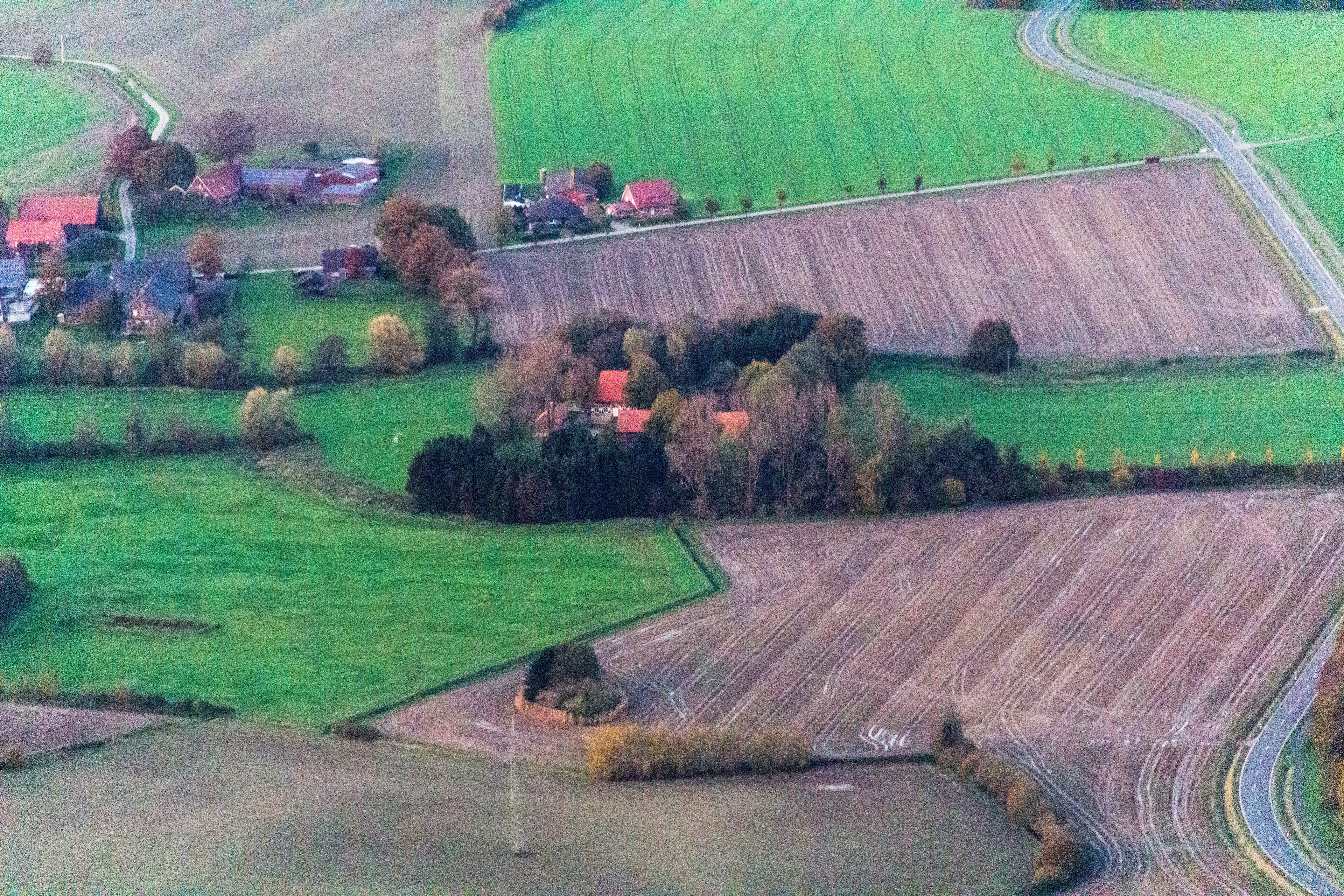 An aerial view of a rural landscape with fields, a winding road, and several red-roofed houses.