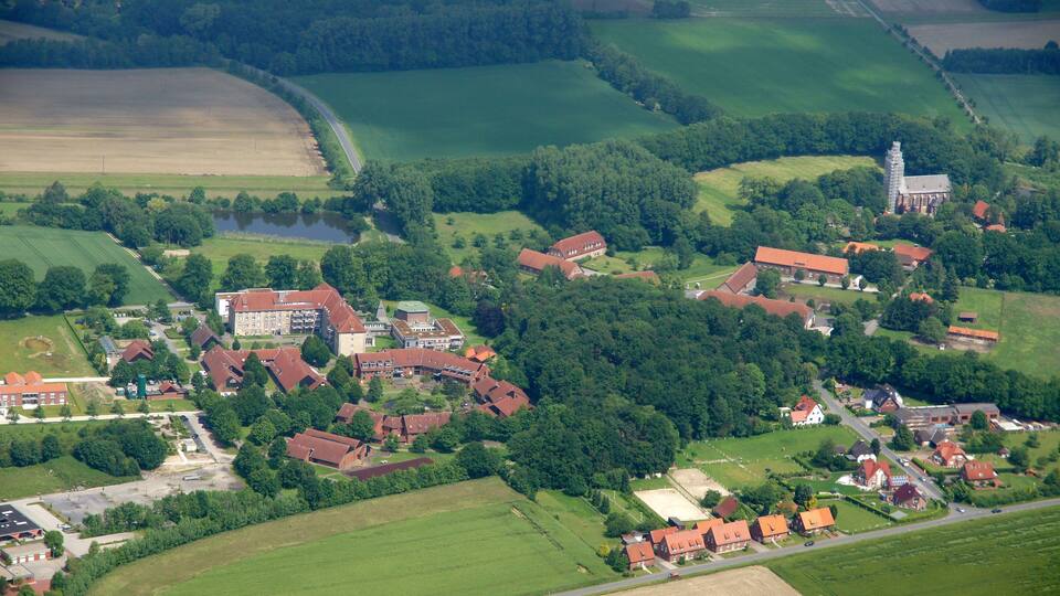 An aerial view of a rural village with red-roofed houses, a church, and surrounding fields.
