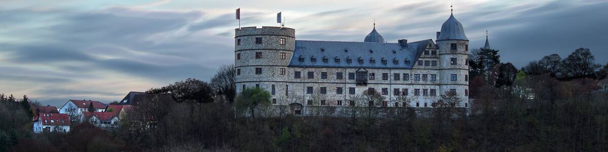 Eine große Steinschlossburg mit mehreren Türmen und einer steilen Anhöhe im Vordergrund.