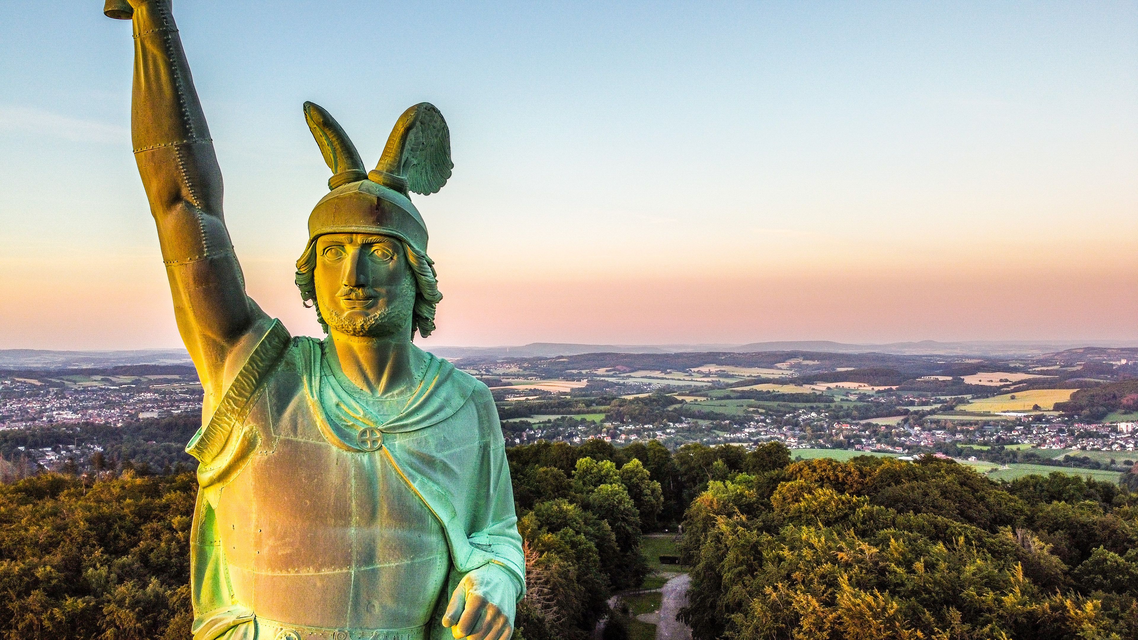 A statue of a figure with raised arm, set against a backdrop of a town and countryside.