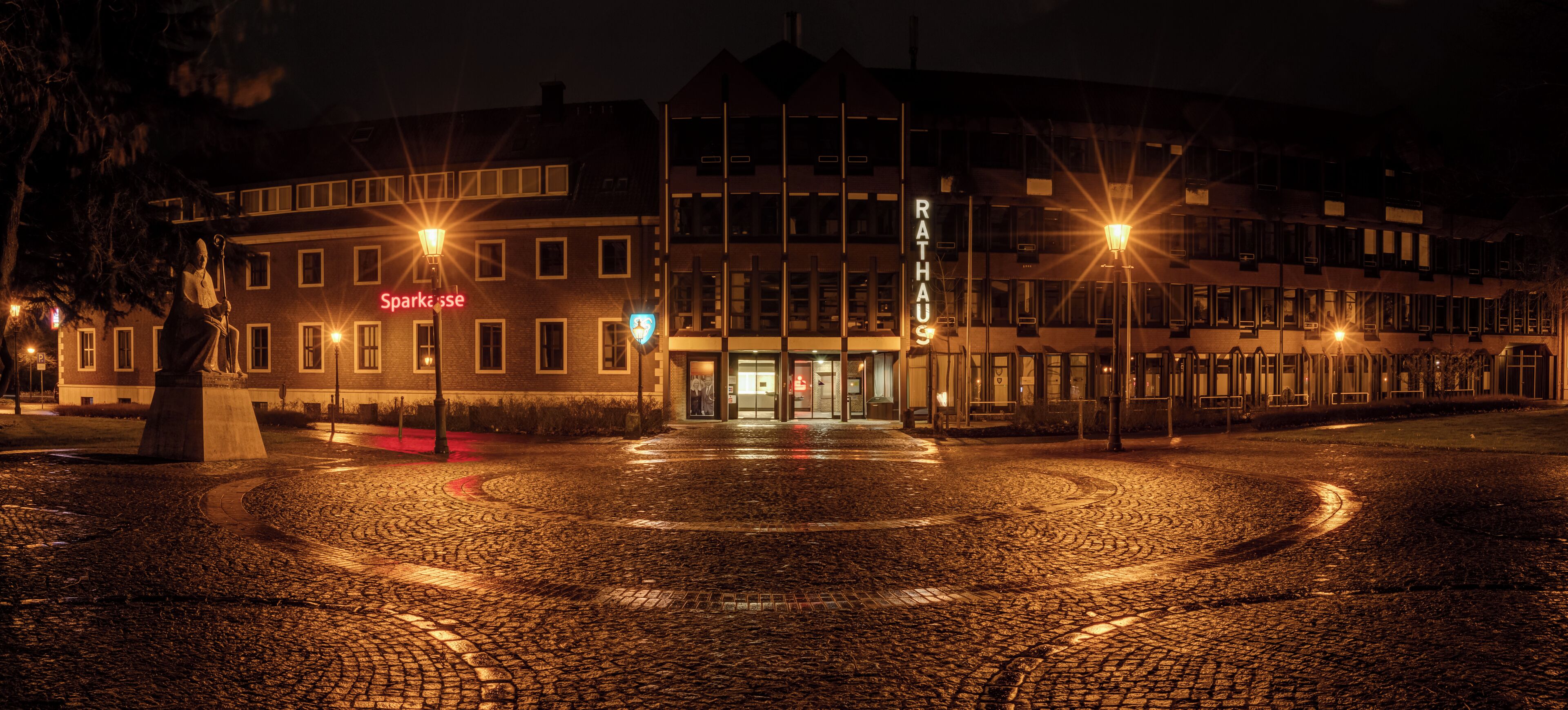 A cobblestone square with a statue, a building with 'RATHAUS' sign, and a 'Sparksse' sign.