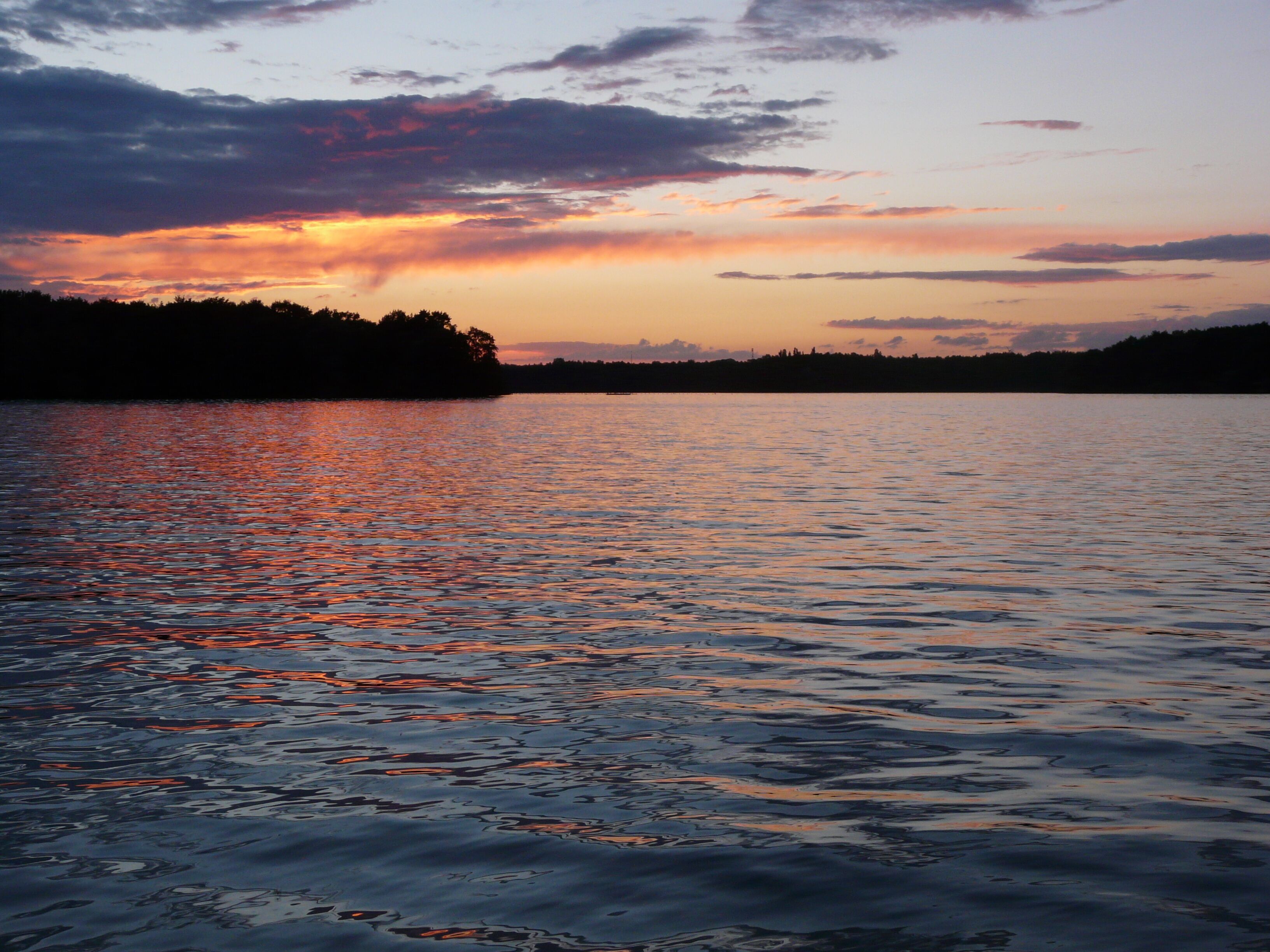 A sunset over a calm lake with a silhouette of trees on the horizon.