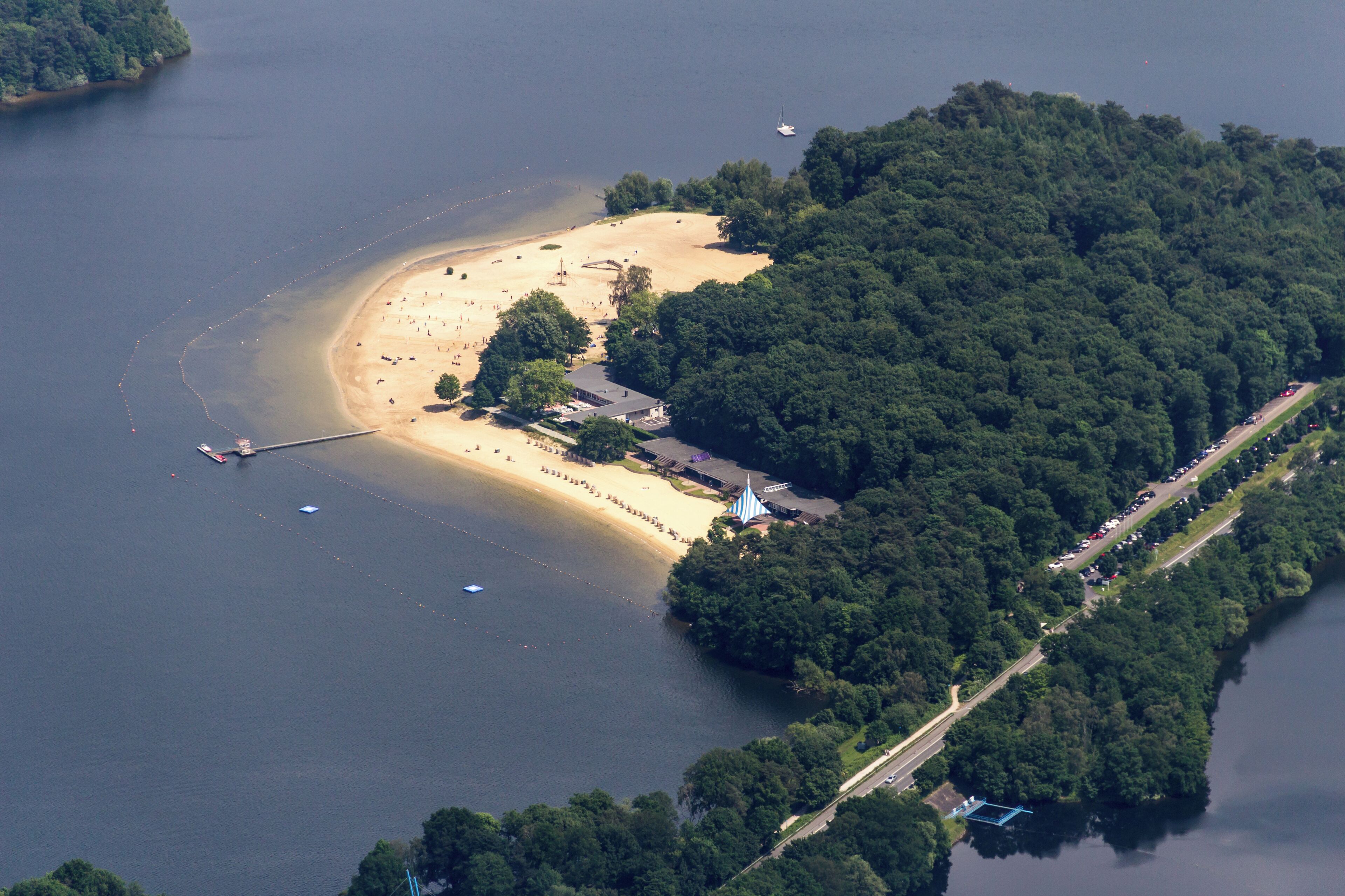 An aerial view of a beach surrounded by dense forest, with a boat dock and a small pier.