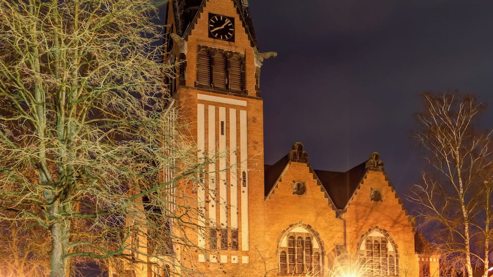 A church with a tall spire and a clock tower at night.