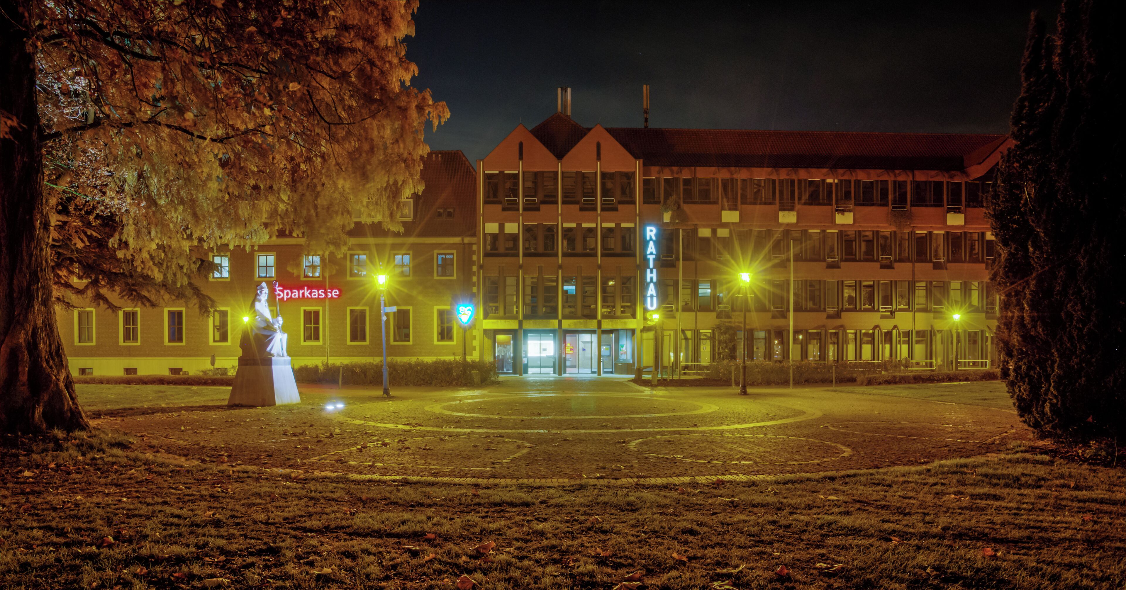 A nighttime view of a building with a sign reading "RATHA" and a statue in the foreground.