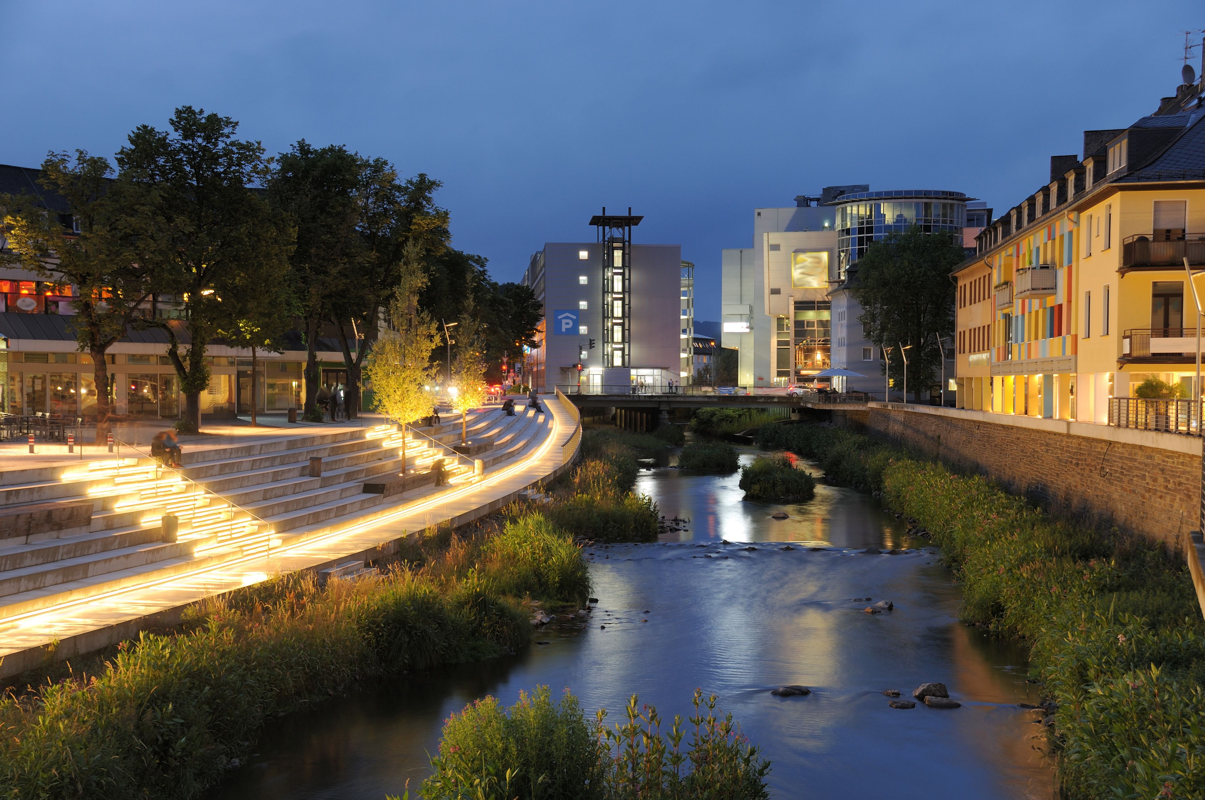 A riverside walkway with steps, a bridge, and modern buildings.