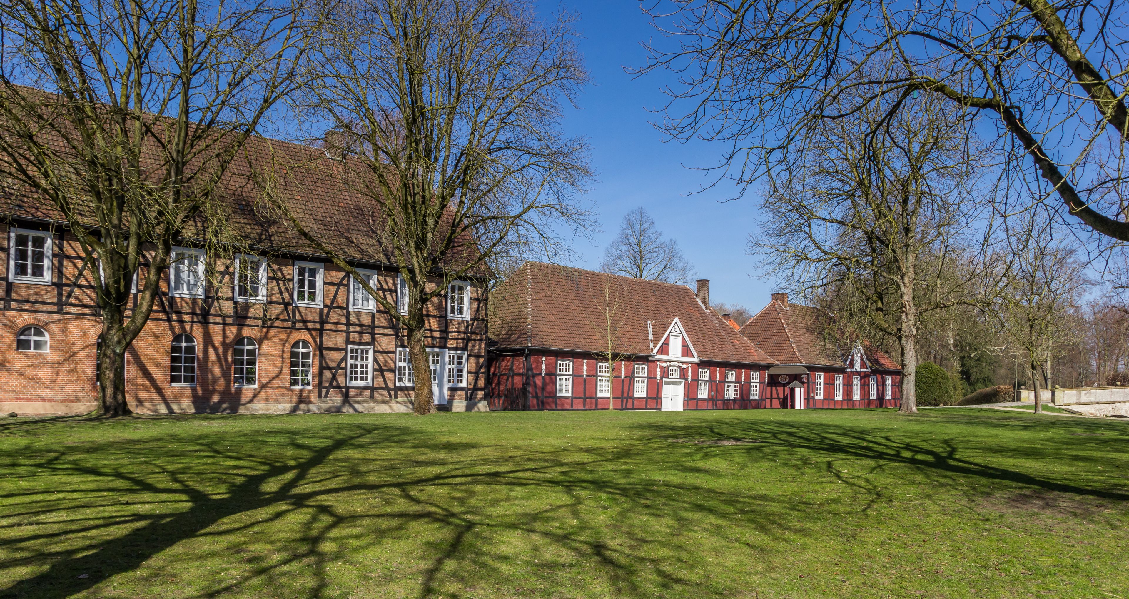 Ein traditionelles Fachwerkhäuschen mit roter Fassade und weißem Zierrat, umgeben von einem gepflegten Rasen und kahlen Bäumen.