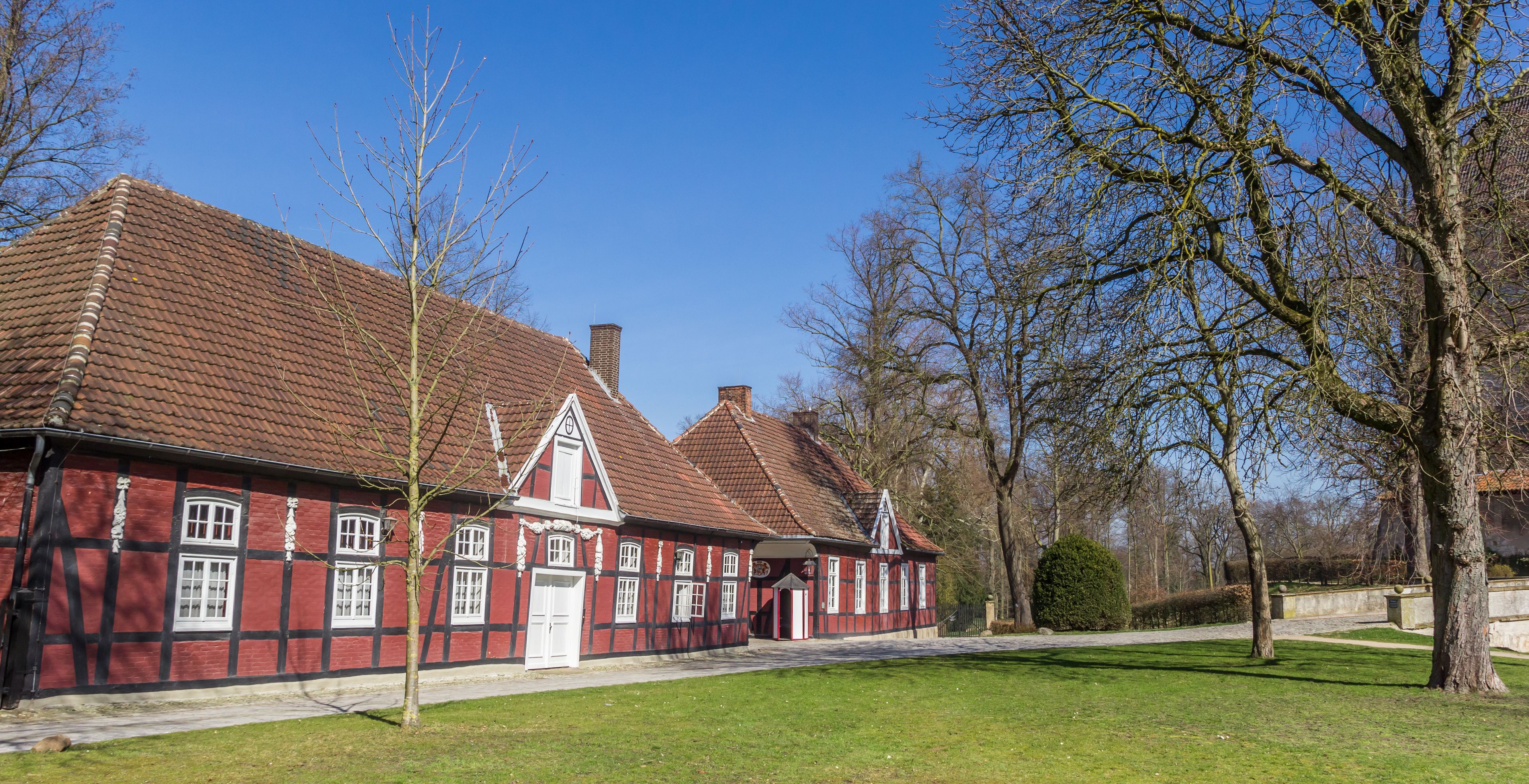 Ein rotes Gebäude mit einem Ziegeldach und weißer Verzierung, umgeben von einer Rasenfläche und Bäumen.