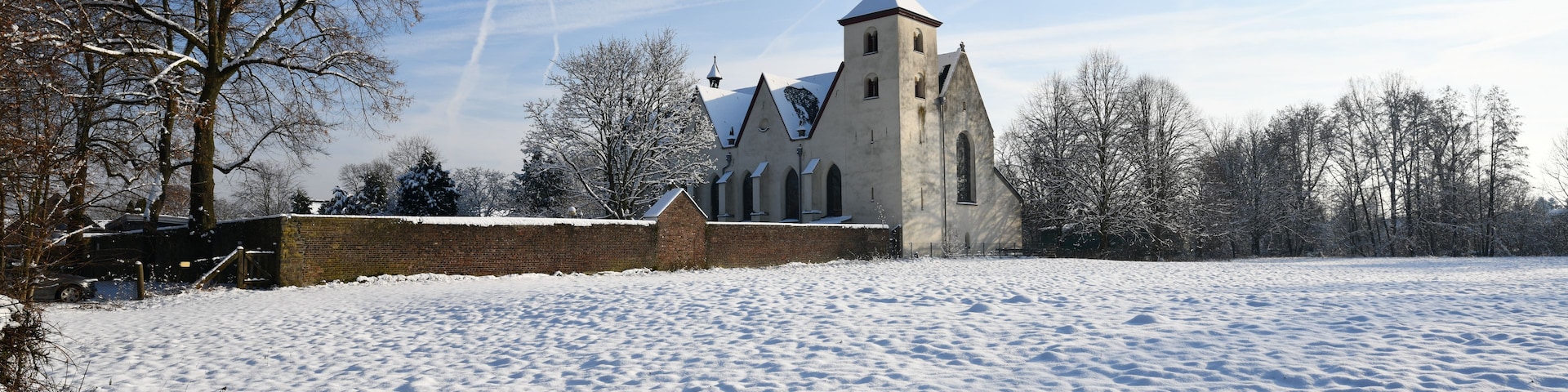 Un champ enneigé avec une église et des arbres sans feuilles.