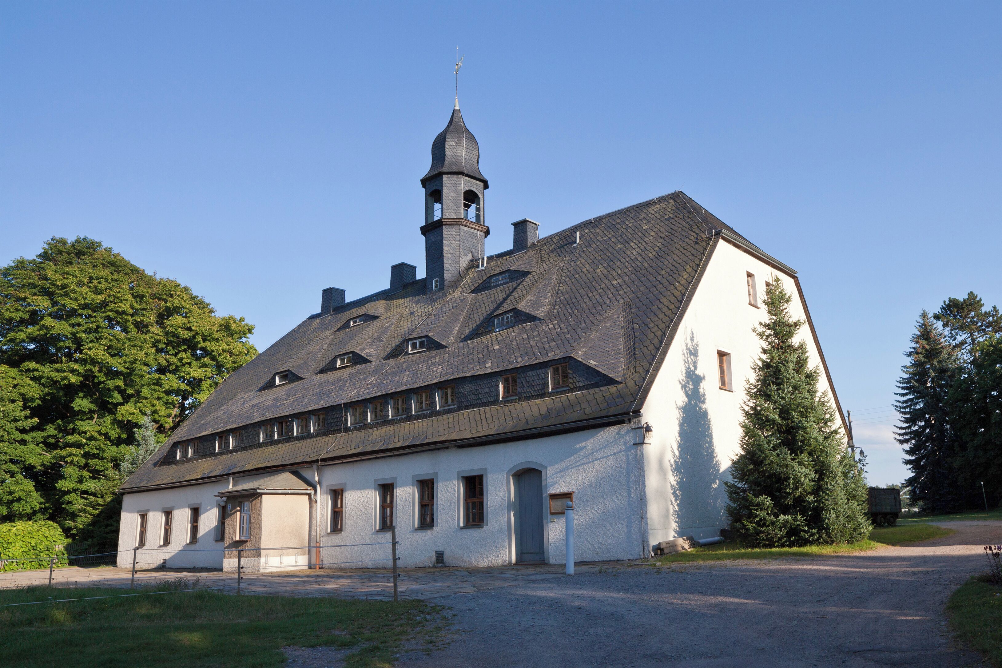 A large white building with a steeply pitched roof and a tower.