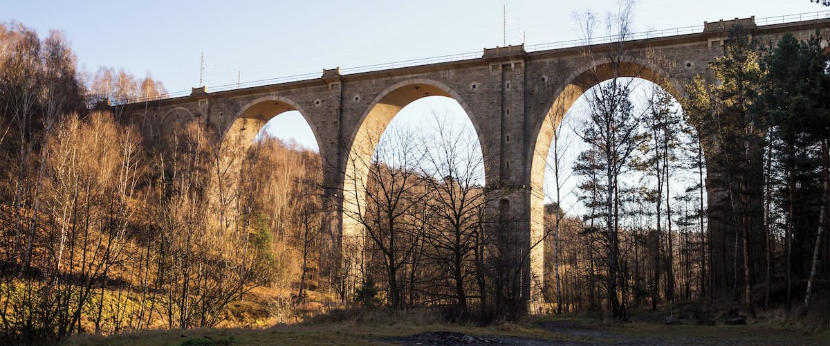 A stone bridge with multiple arches over a forested area.