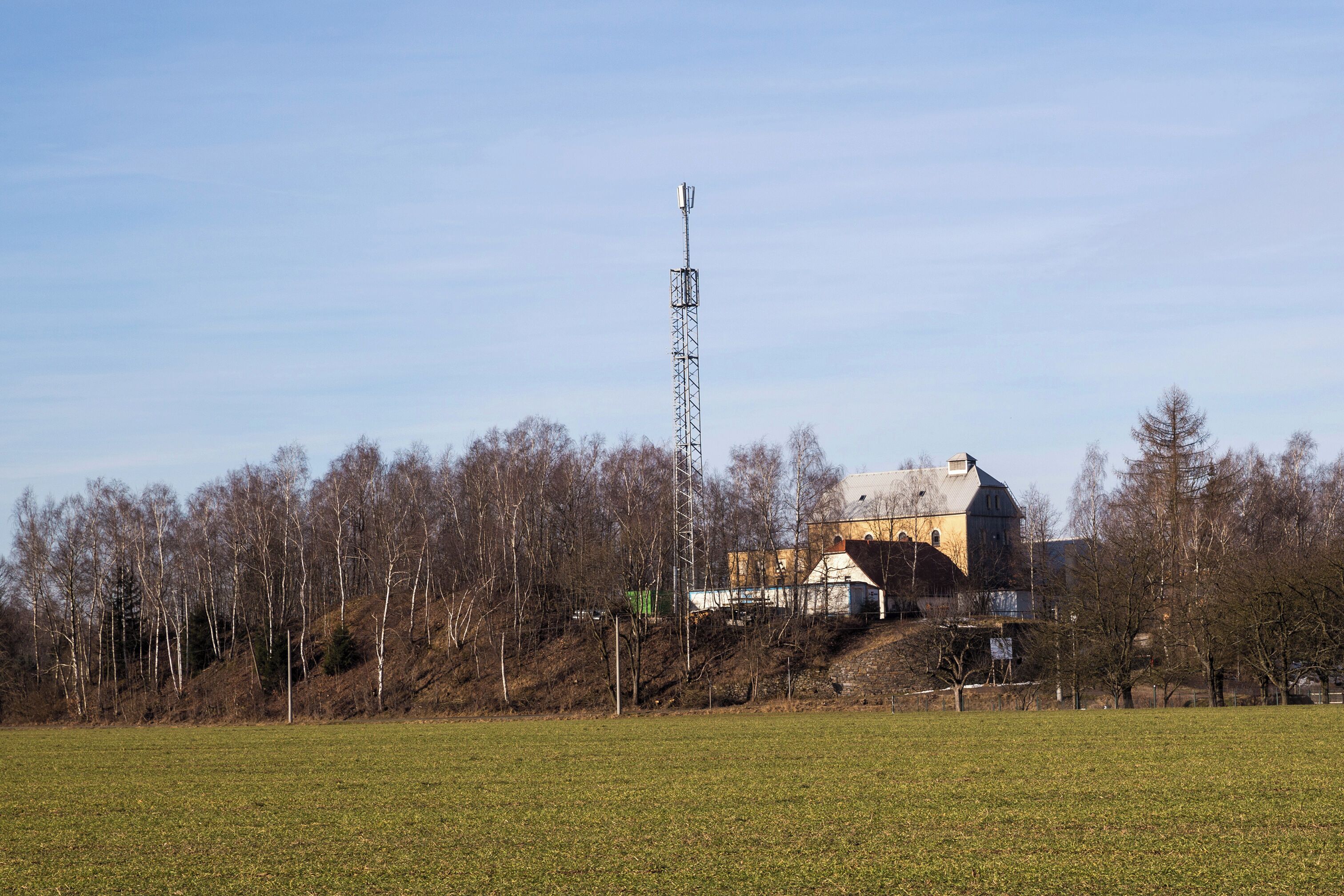 A rural landscape with a large building, a tall communication tower, and a field.
