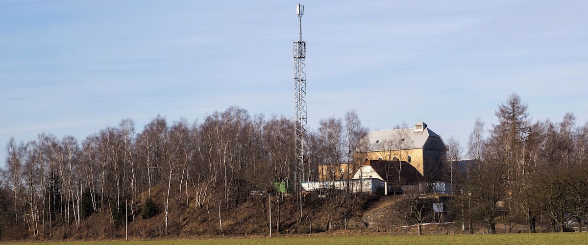 A rural landscape with a large building, a tall communication tower, and a field.