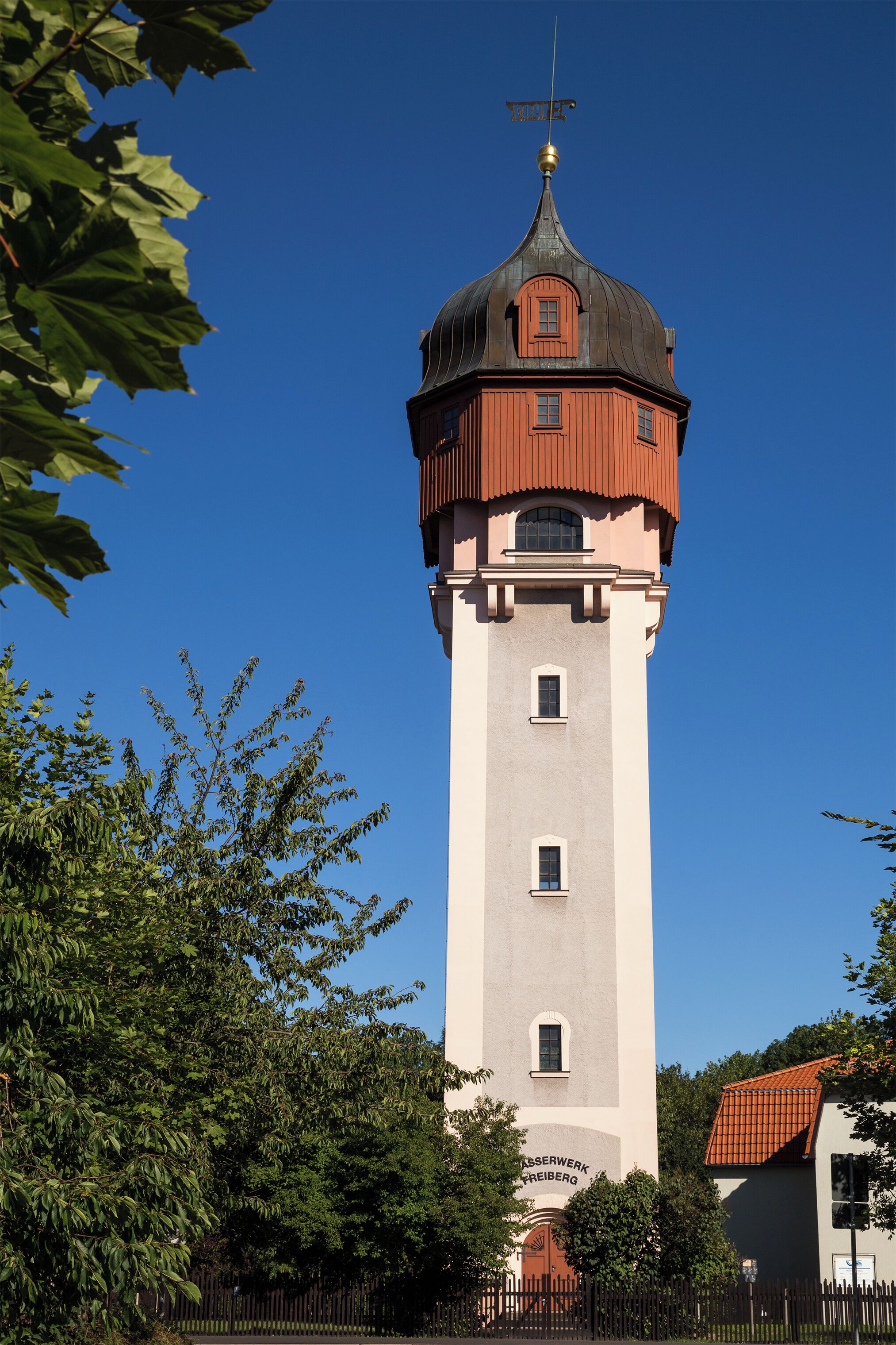 A tall tower with a red roof and a weather vane, surrounded by trees.