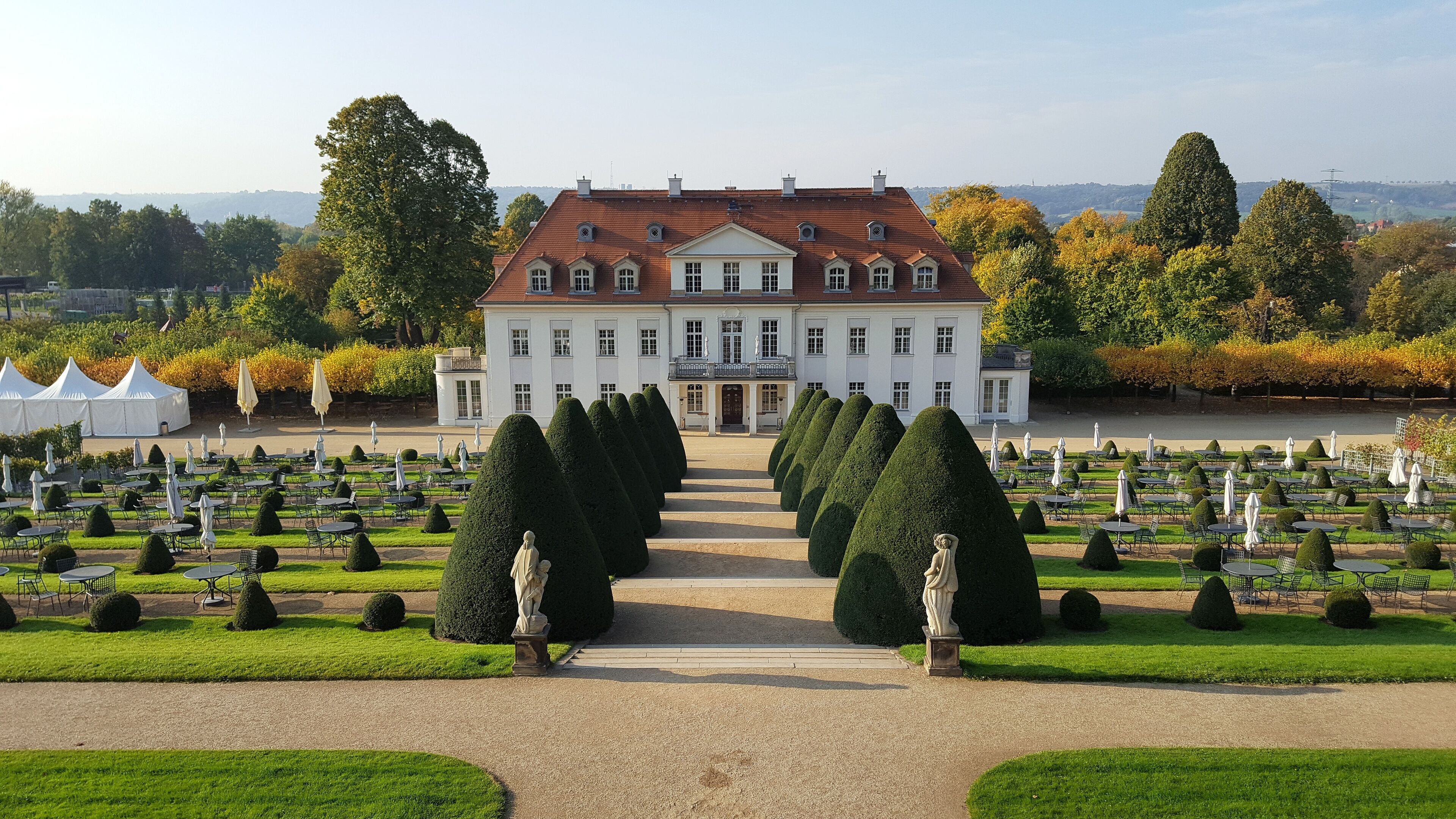 A grand building with a symmetrical facade, surrounded by a formal garden with neatly trimmed hedges and a central pathway leading to the entrance.