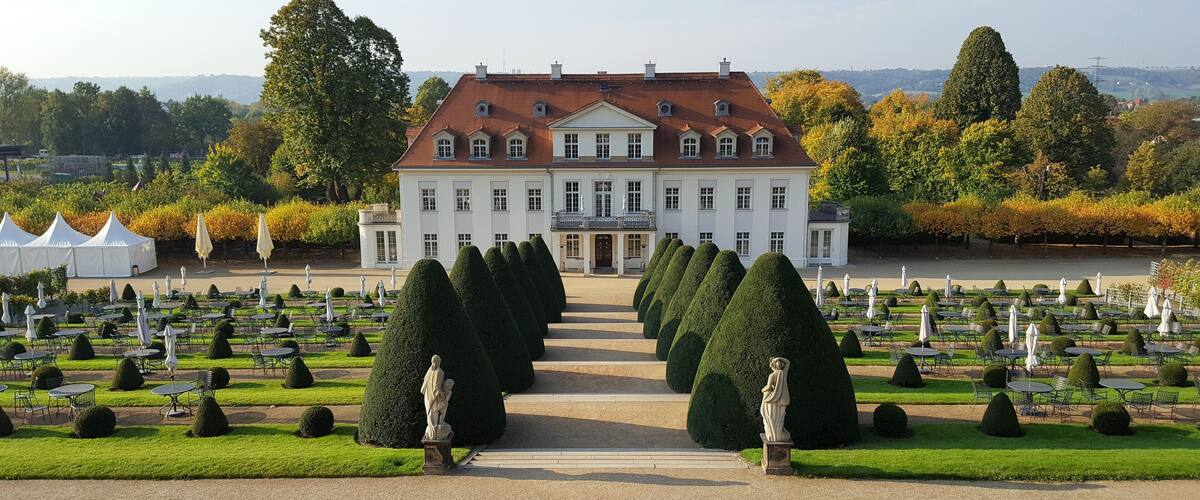 A grand building with a symmetrical facade, surrounded by a formal garden with neatly trimmed hedges and a central pathway leading to the entrance.
