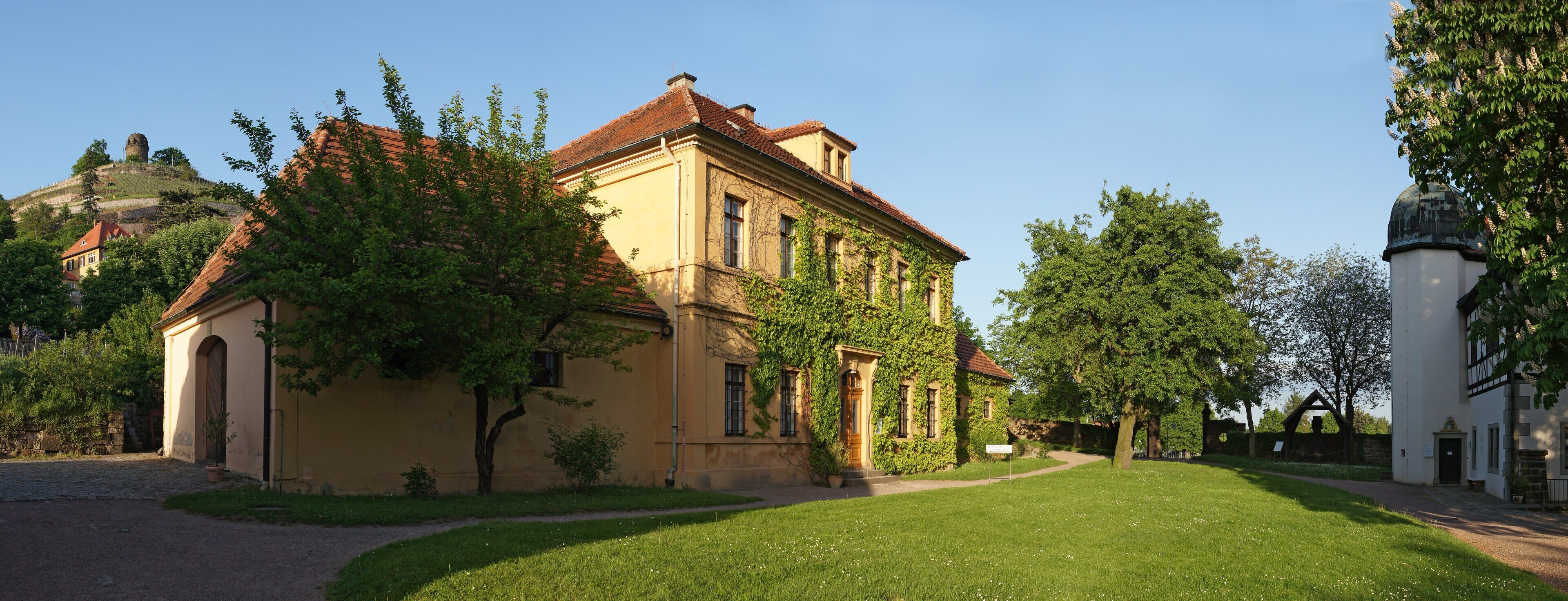 A historic building with ivy-covered walls, a red-tiled roof, and a small tower in the background.