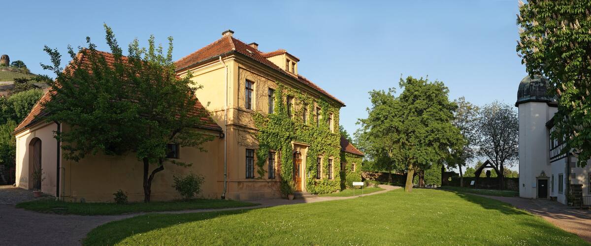A historic building with ivy-covered walls, a red-tiled roof, and a small tower in the background.