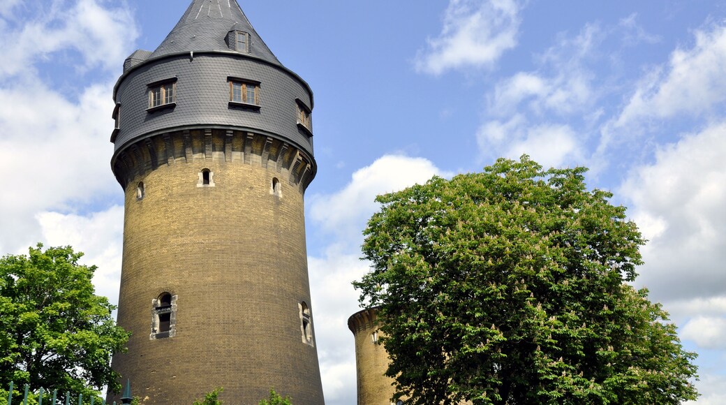 A historic tower with a conical roof and a brick base, surrounded by lush green trees.