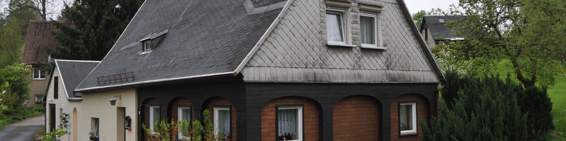 A house with a steeply pitched roof, a small attached garage, and a well-maintained hedge in front.