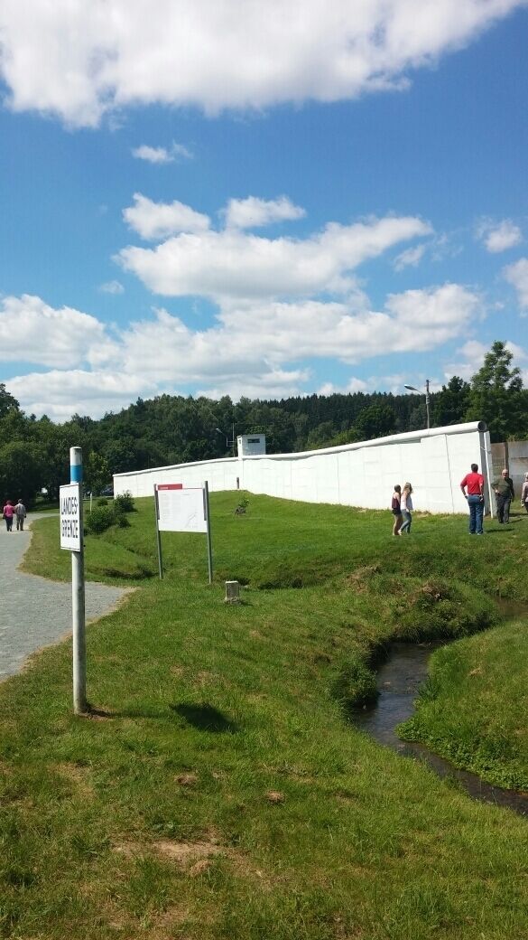 A grassy area with a white wall, a small stream, and a signpost.