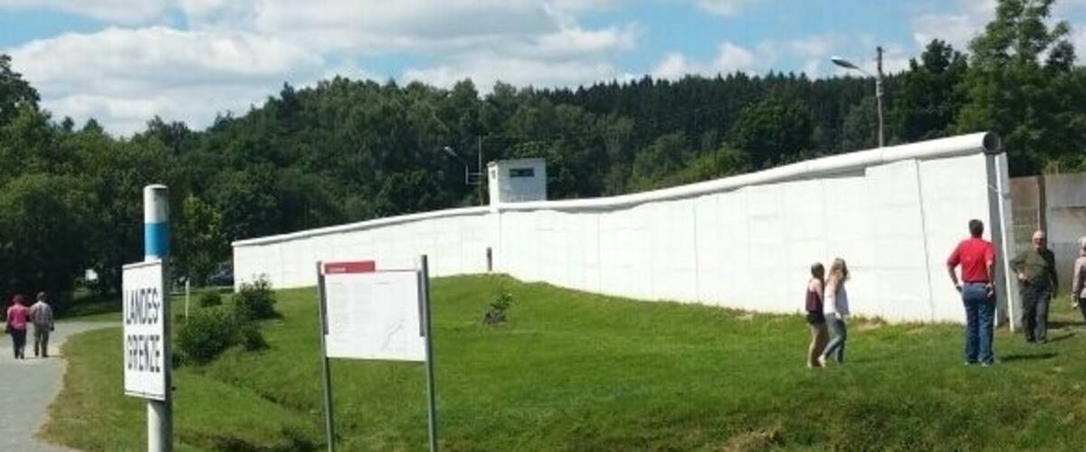 A grassy area with a white wall, a small stream, and a signpost.