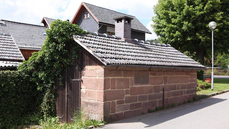 A traditional stone building with a tiled roof and a wooden fence.