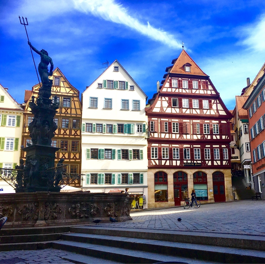A town square with traditional half-timbered houses, a statue, and cobblestone pavement.