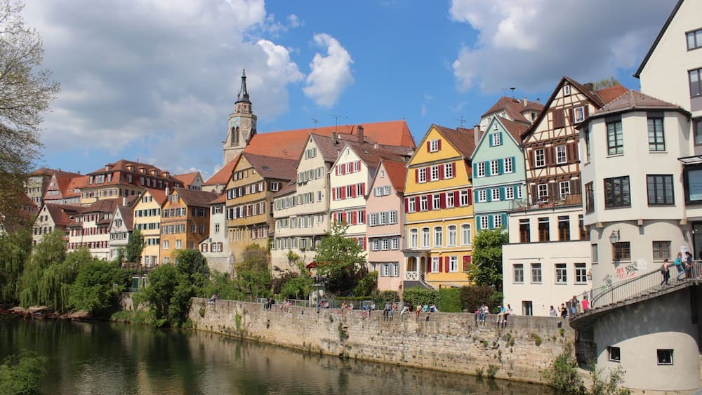 A river with colorful buildings along the banks, a stone bridge, and a church tower.