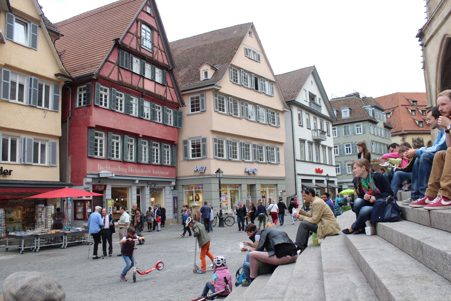 Una plaza europea animada con edificios históricos, un vendedor de libros y gente realizando diversas actividades.