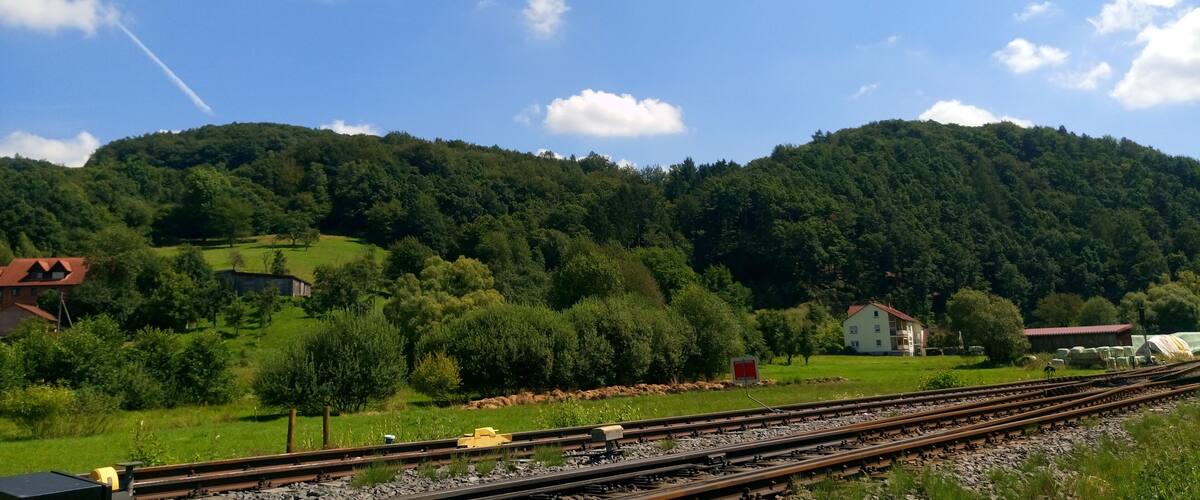 A rural landscape with a railway track, green fields, and a hill with trees.