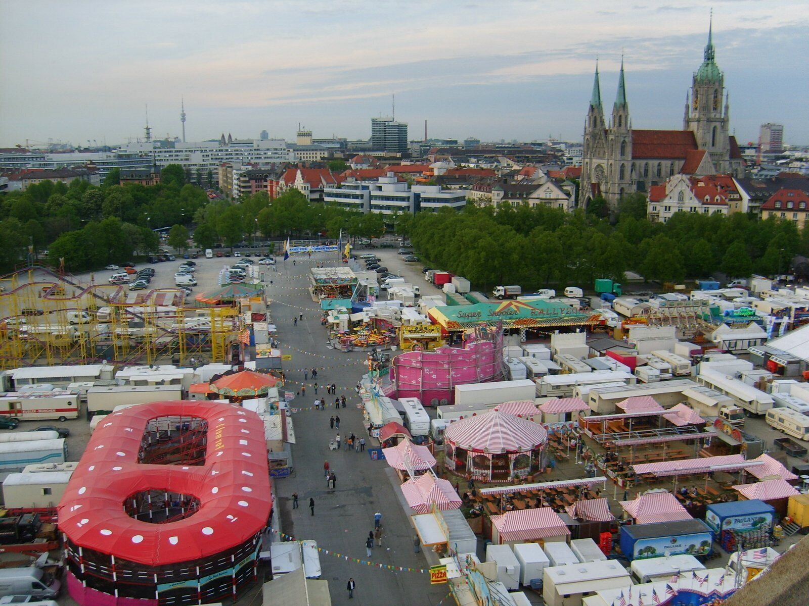 A bustling outdoor market with various stalls and tents, surrounded by buildings and a prominent church tower in the background.