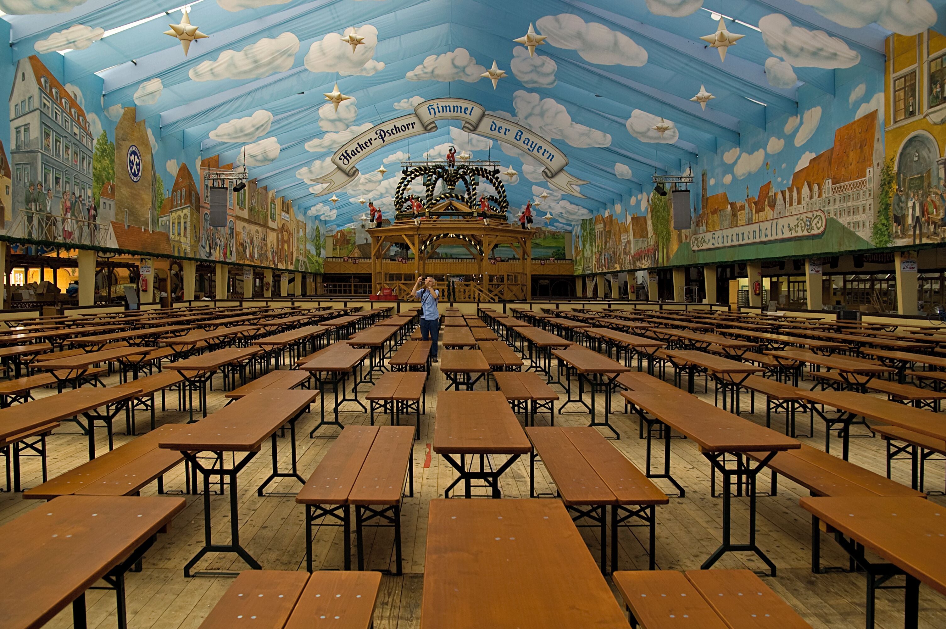 A large hall with wooden tables and a mural of a town on the ceiling.