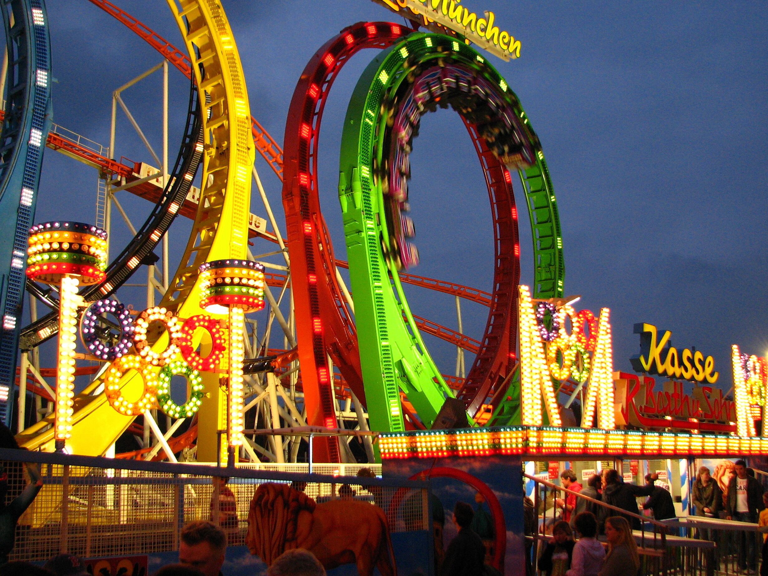 A brightly lit amusement park with roller coasters and a sign that reads "Kasse."