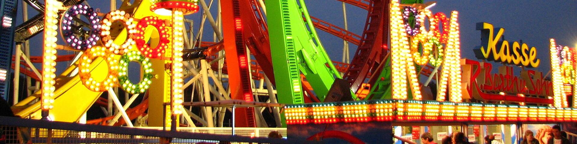 A brightly lit amusement park with roller coasters and a sign that reads "Kasse."