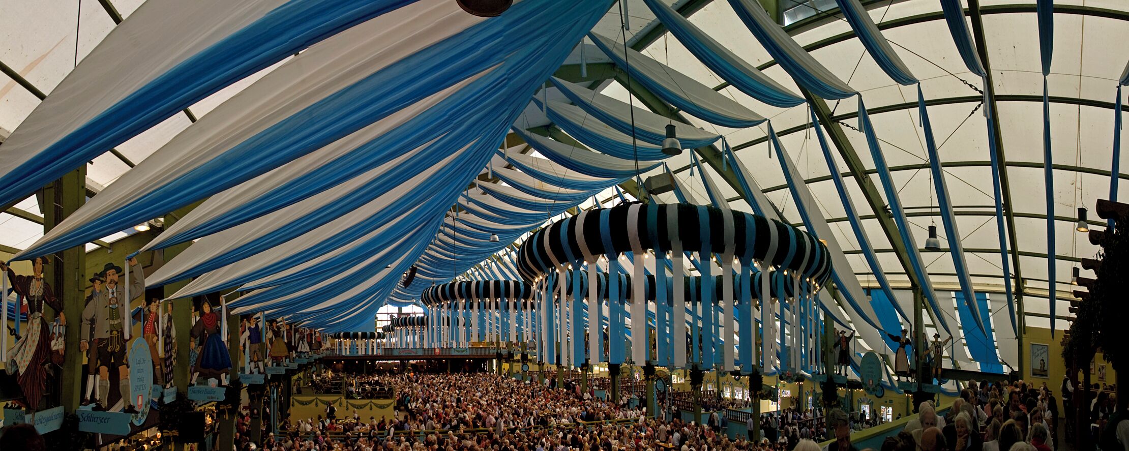 A large indoor market with blue and white drapes, a crowd of people, and various stalls.