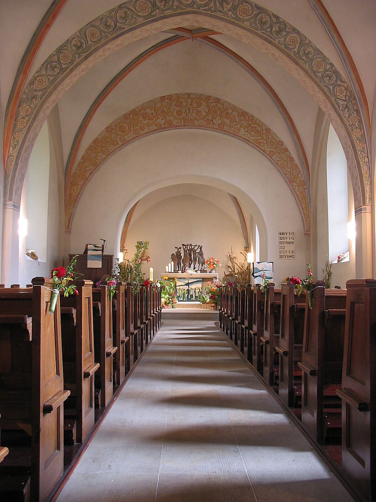 An aisle with wooden pews, floral decorations, and a central altar with statues.